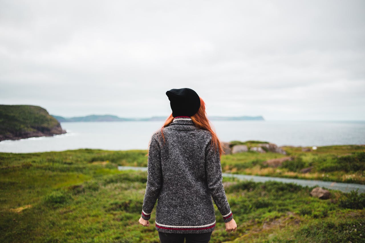 Woman with red hair stands in solitude, enjoying the scenic coastal view.
