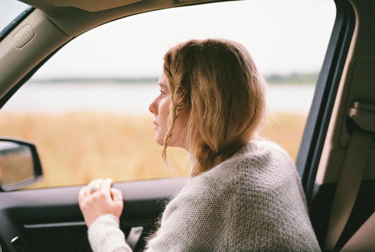 Woman sitting in car looking out the window, captured in a thoughtful moment during a road trip.